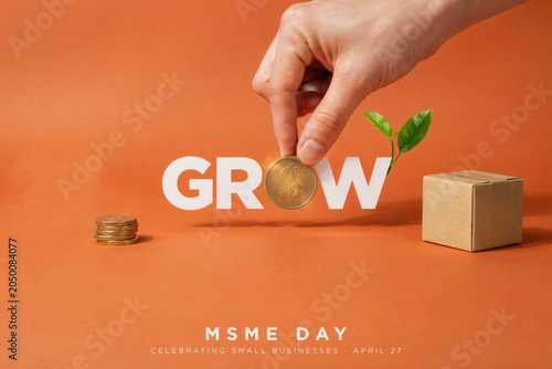 A hand placing a coin into the word 'GROW' with a plant sprouting near a block and coins on an orange background for MSME Day.