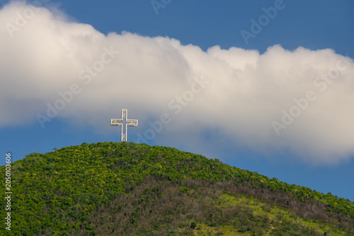 Cuadro en lienzo Large white cross standing on green hilltop beneath dramatic clouds and blue sky
