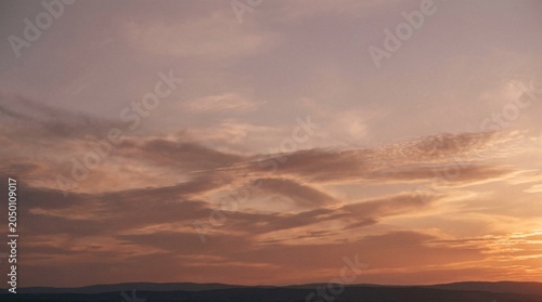 Beautiful Atmospheric Sunset Sky Background Featuring Soft Pastel Clouds and Gradient Hues Over a Distant Horizon at Golden Hour