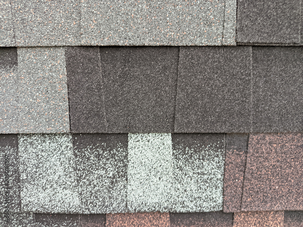 Fototapeta premium Detailed top-down view of overlapping asphalt roof shingles featuring a gritty, mineral-granule texture in various shades