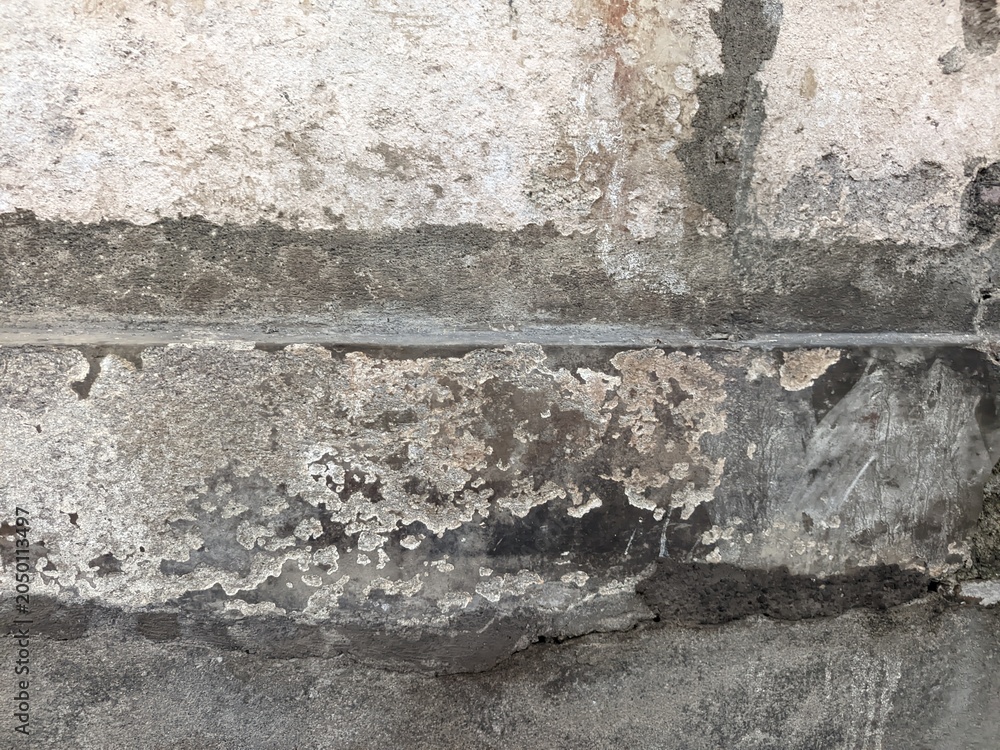 Fototapeta premium A close-up shot of a badly damaged concrete wall with a large hole, deep cracks, peeling plaster, and white liquid drip stains.