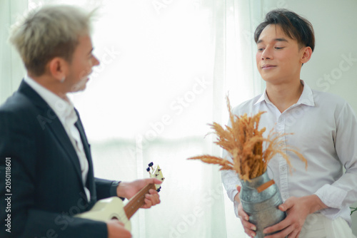Fotografia Gay male couple uses persuasive language and flirting impress and capture the other's attention during intimate activities at home such as playing the ukulele showcase their talents