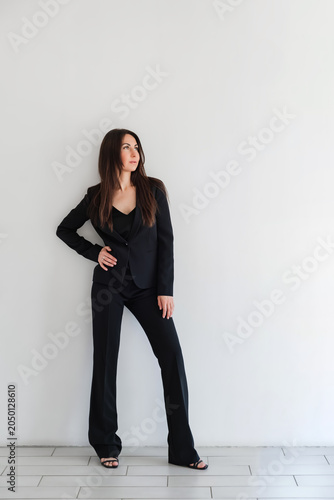 Photos Woman looking side in black formal pantsuit or suit stands against white wall in studio