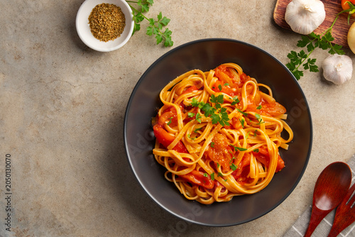 Fettuccine pasta with fresh tomatoes sauce in black plate.topped with parmesan cheese and parsley.Top view.