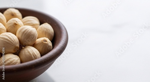 A brown bowl filled with hazelnuts sits on a white surface in a well-lit indoor setting.