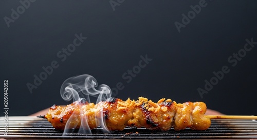 Grilled meat skewer sizzles on a metal grill over a dark background with smoke rising.