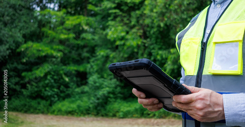 Obraz na plátně Forestry engineer or ecologist holding digital tablet in protective rugged case during field research in green forest