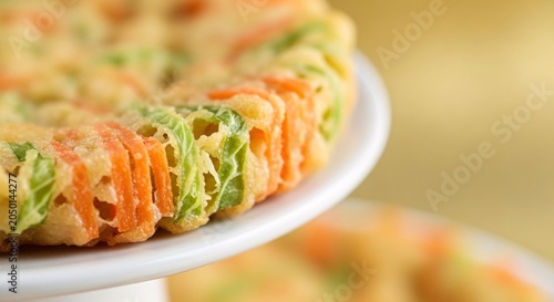 Delicious colorful vegetable quiche on a white plate with another quiche in background on table indoors