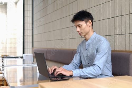 Young Man Working Remotely on Laptop in Modern Cafe Workspace Concentrated on Task