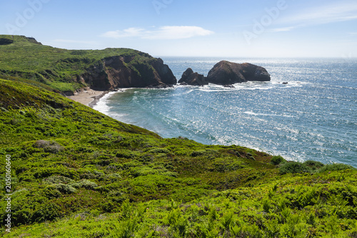 Scenic view of Rodeo Beach and sea stacks in Marin Headlands, California, lush green coastal hills overlooking Pacific Ocean along Highway 1 on a bright sunny day