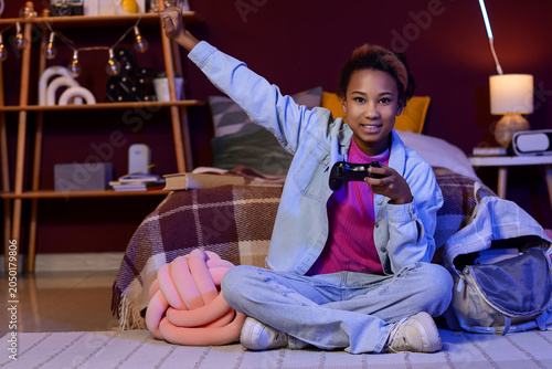 Teenage African-American girl playing video game in bedroom at night