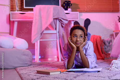 Thoughtful teenage African-American girl doing homework in bedroom