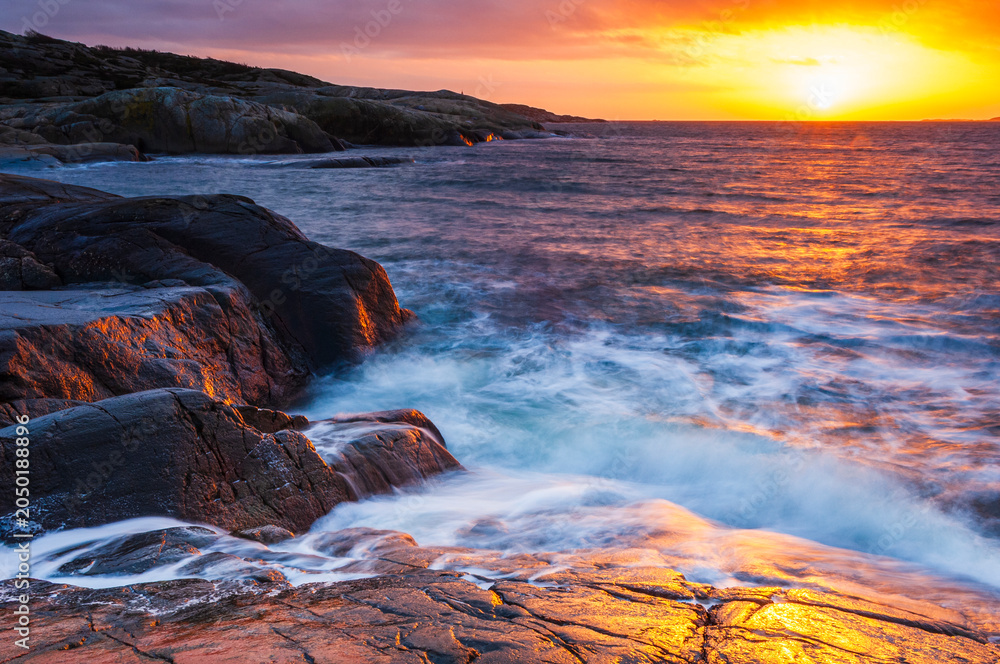 Obraz premium Coastal sunset view near Gothenburg in Sweden with waves crashing on rocks