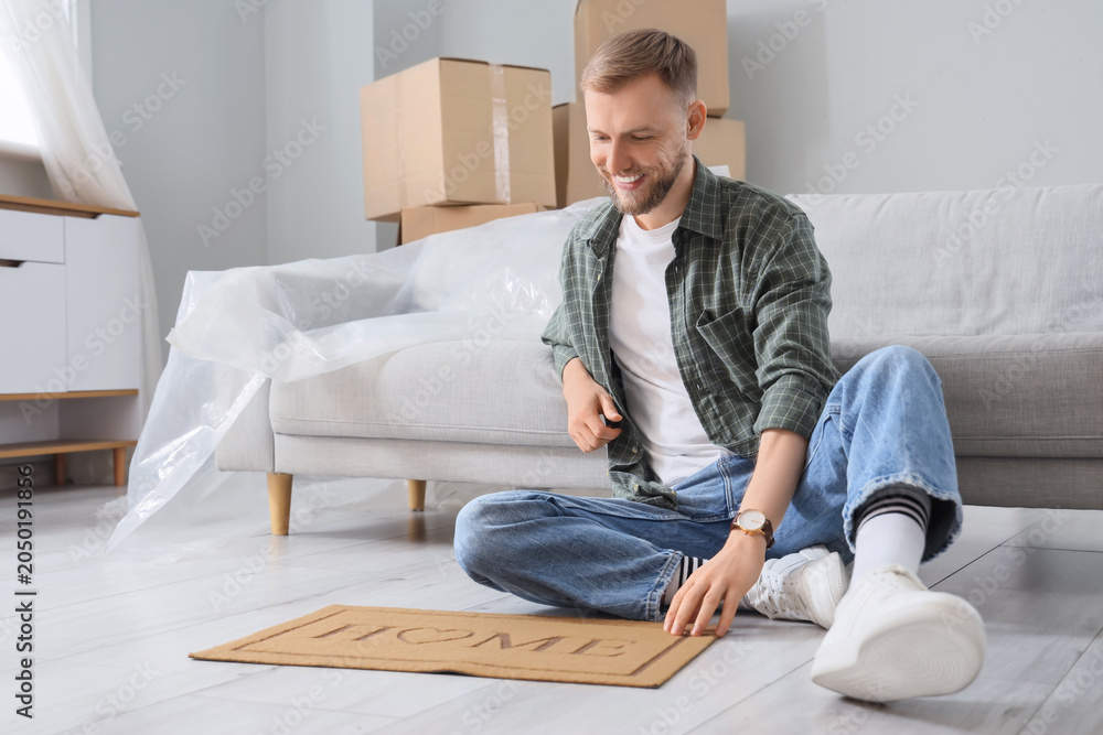 Fototapeta premium Young man with doormat sitting in room on moving day