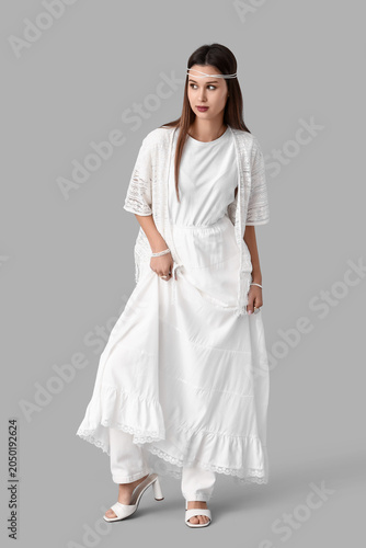 Young woman in stylish white clothes on grey background