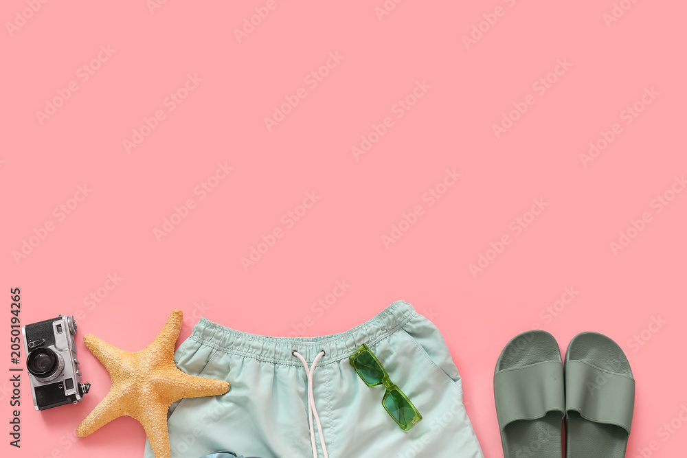 Obraz premium Swimming trunks with beach accessories and photo camera on pink background