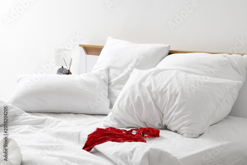 Interior of hotel room with unmade bed  crumpled linen and female underwear near white wall
