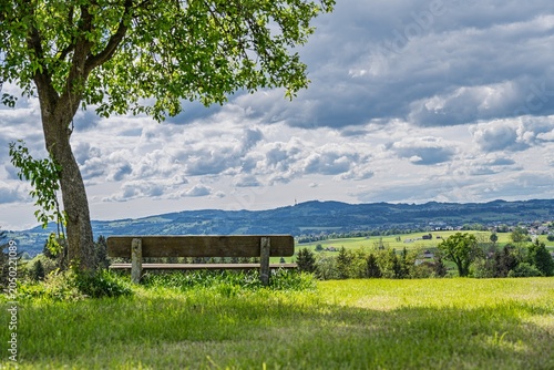 Wooden Bench under Tree with Scenic View towards Blender Mountain near Betzigau and Kempten, Idyllic Alpine Meadow Landscape and Rural Panorama under Dramatic Sky in Allgau Bavaria Germany in Summer
