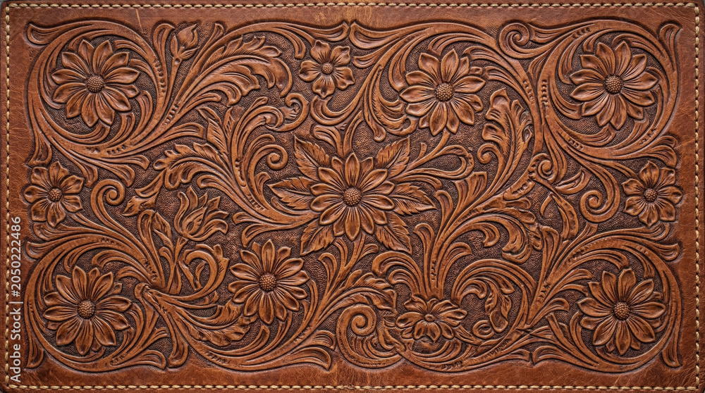 Naklejka premium Western hand tooled leather panel with embossed floral scroll pattern and visible stitching border in warm brown tones