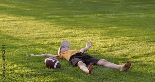 Child lies relaxed on grass in sunny park. Child while resting after sport. Child enjoys nature fresh air outdoors. Kid feels happy calm outdoors. Boy embraces healthy lifestyle. Wellness, family time