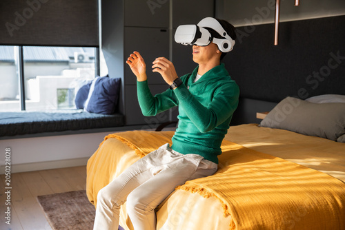 White VR headset with headphones is resting on bed with mustard-yellow blanket, sunlight streaming
