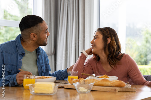 Mid-adult couple sitting at wood table by windows sharing breakfast with bowls and orange juice
