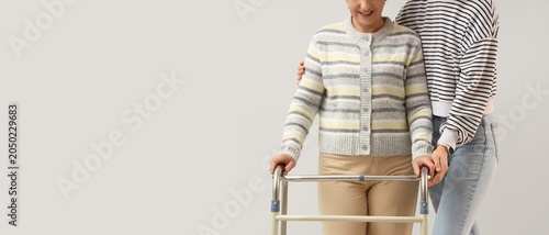Tableau sur toile Smiling senior woman using walker with supportive caregiver or daughter at home,