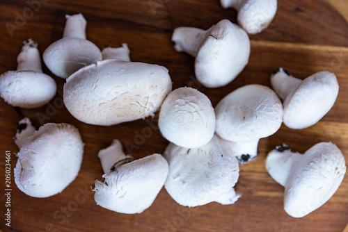 Fresh raw white Agaricus mushrooms on a wooden cutting board