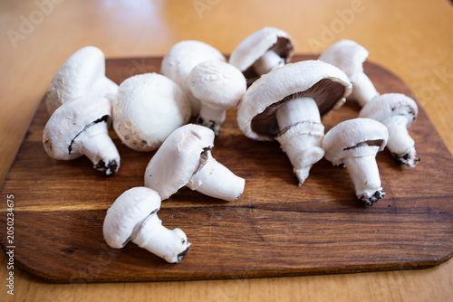 Fresh white Agaricus mushrooms on a wooden cutting board