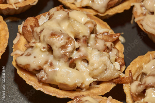 Homemade tartlets filled with chanterelle mushrooms and chicken pieces stewed in cream, topped with grated cheese after baking in oven. Close-up of a festive appetizer cooking process.