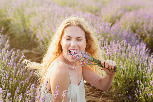 Quadro em tela Playful woman pretending to bite lavender bouquet in blooming field, joyful mood