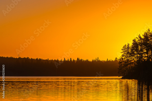 Sunrise at a lake near Gothenburg in Sweden with trees along the shoreline and a bright orange sky