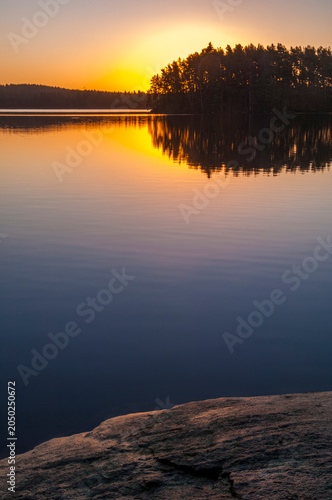 Sunrise at a lake outside Gothenburg in Sweden with calm waters and trees reflecting on the surface