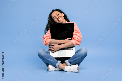 Konstfotografi A woman sits on the floor with her legs crossed and hugs a laptop