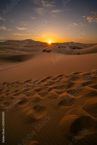 Golden sunset over the sand dunes of the Sahara Desert in Morocco. Dramatic desert landscape with rippled sand, warm sunlight and endless wilderness.