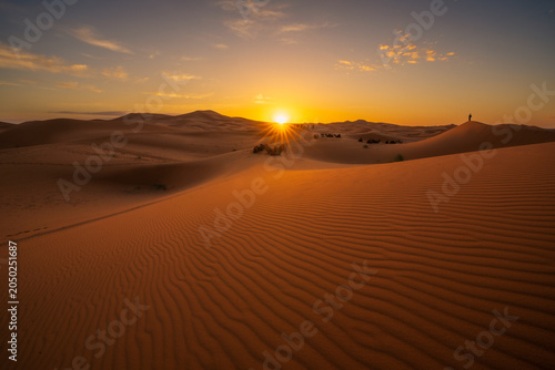Golden sunset over the sand dunes of the Sahara Desert in Morocco. Dramatic desert landscape with rippled sand, warm sunlight and endless wilderness.