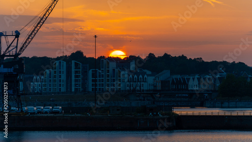 фотографія Orange sunset with the sun halfway below the horizon behind houses, creating a warm evening sky and dramatic silhouette