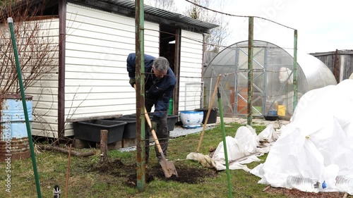 A gardener plants a bush in a garden bed in a park. A gardener plants a plant in a garden plot.