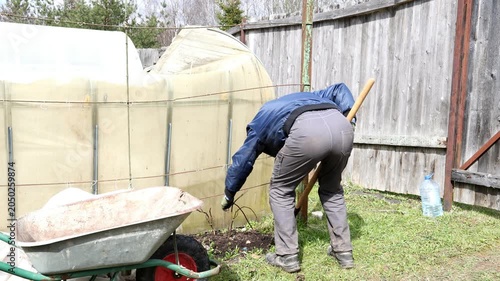 A gardener plants a bush in a garden bed in a park. A gardener plants a plant in a garden plot.