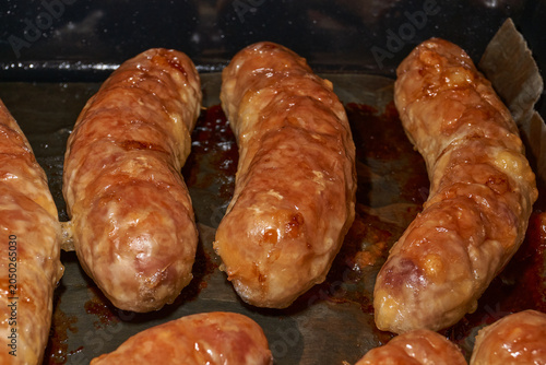 Hot homemade sausages with a juicy texture and golden surface on a parchment-lined baking tray. Golden Brown Pork Sausages Fresh from the Oven. Baked Homemade Sausages Close Up.