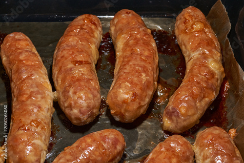 Hot homemade sausages with a juicy texture and golden surface on a parchment-lined baking tray. Golden Brown Pork Sausages Fresh from the Oven. Baked Homemade Sausages Close Up.