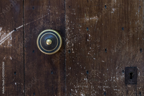 A brass doorbell button and keyhole on a heavily weathered and scratched dark wooden door in a French village