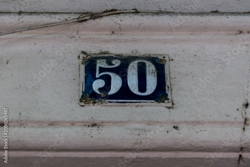 A ceramic house number 50 plaque with blue numerals on a cream tile, mounted on a weathered stone wall in a French village