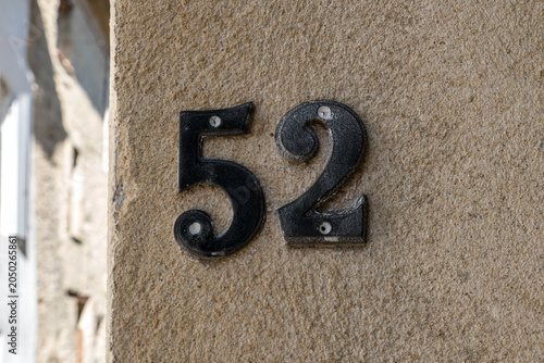 A bold black cast iron house number 52 mounted directly onto a rough sandy, rendered wall in a European village street
