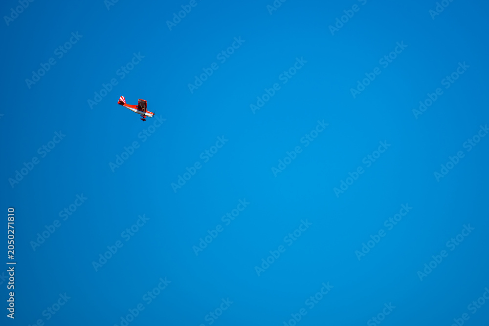 Fototapeta premium Red and white sport airplane flying high in the clear blue sky, minimalist aviation background with vast copy space for text, remote controlled RC plane flight.