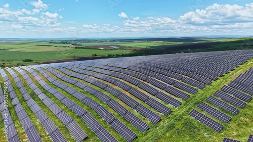 Aerial view solar panels rows sweeping across countryside, precise alignment of photovoltaic modules on gentle slope, green grass interleaving access tracks,