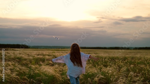 Fotografie Child girl throws toy airplane with hand, child plays in park sunset