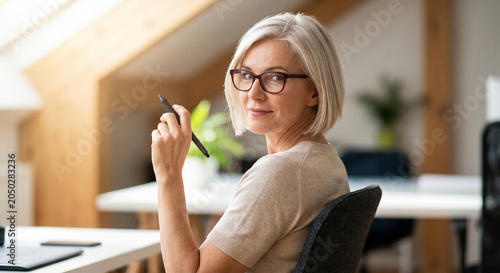 Mature senior designer glancing over shoulder while sketching with stylus pen at loft workstation