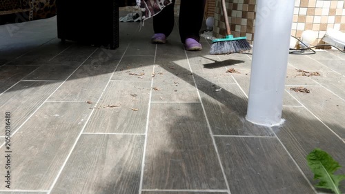A woman removes trash from the floor of a house. A woman sweeps dust from a house.
