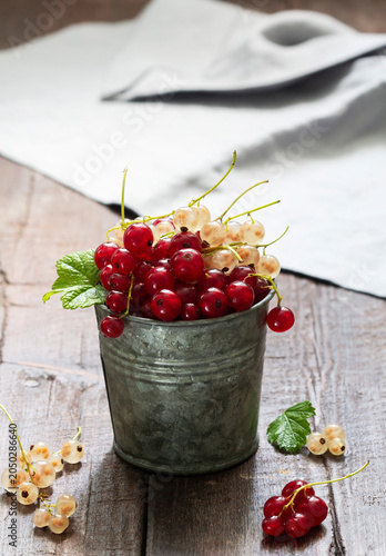White and red currants in a metal bucket on a wooden background.